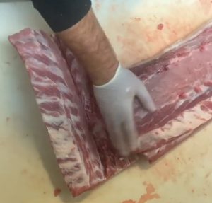 Butcher separating baby back ribs from loin